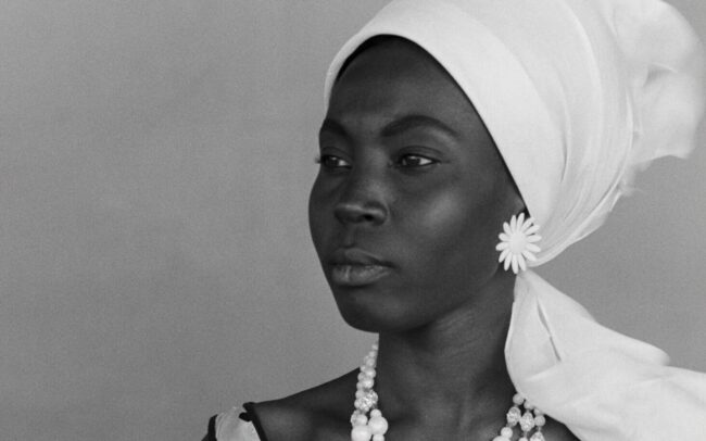 Close portrait of Diouana in a white headscarf, her expression grave and inward, looking past the camera — a still from Black Girl (La Noire de..., 1966) by Ousmane Sembène