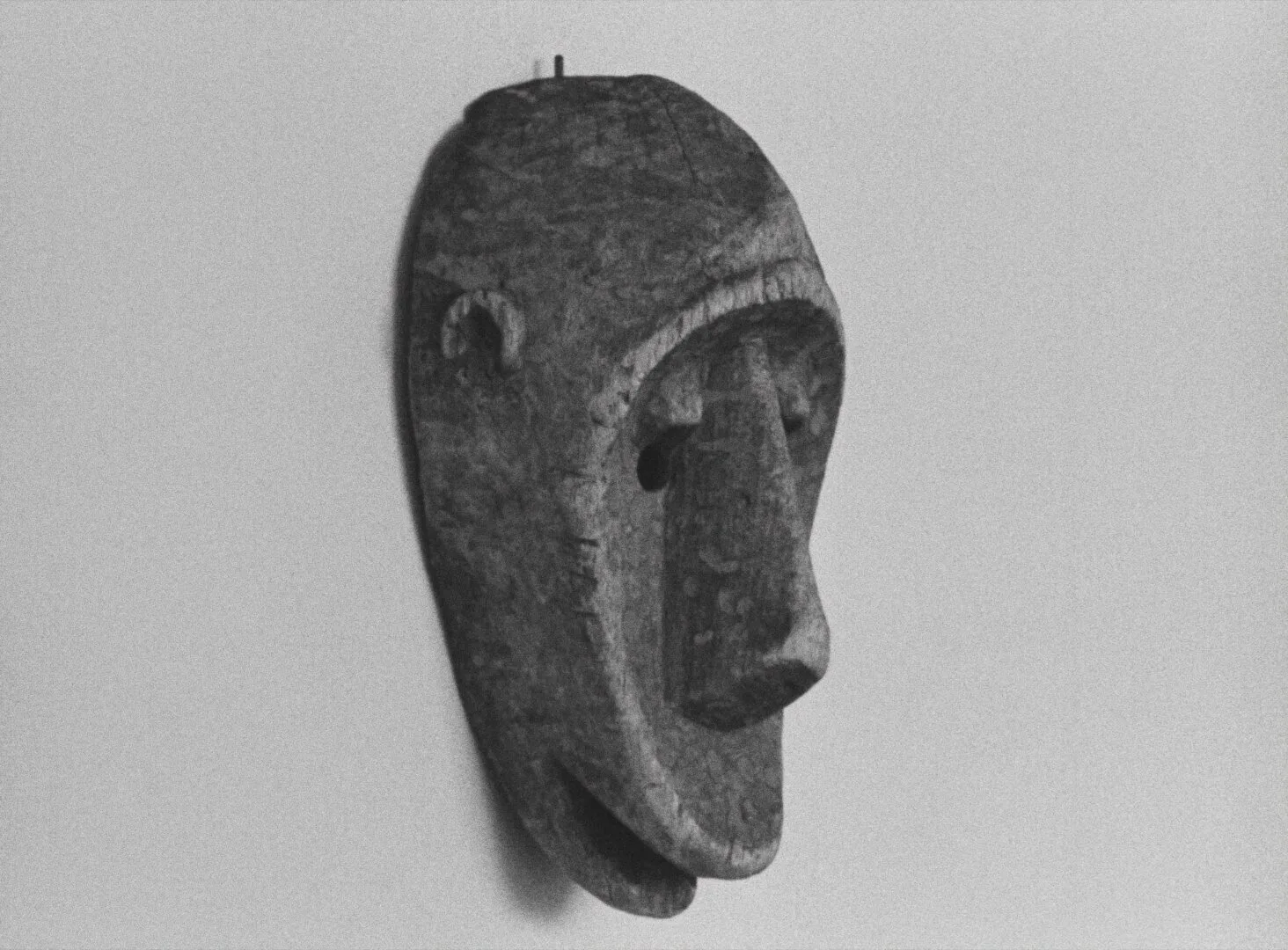 A carved wooden African mask mounted on a plain pale wall, shot in close isolation — a still from Black Girl (La Noire de..., 1966) by Ousmane Sembène