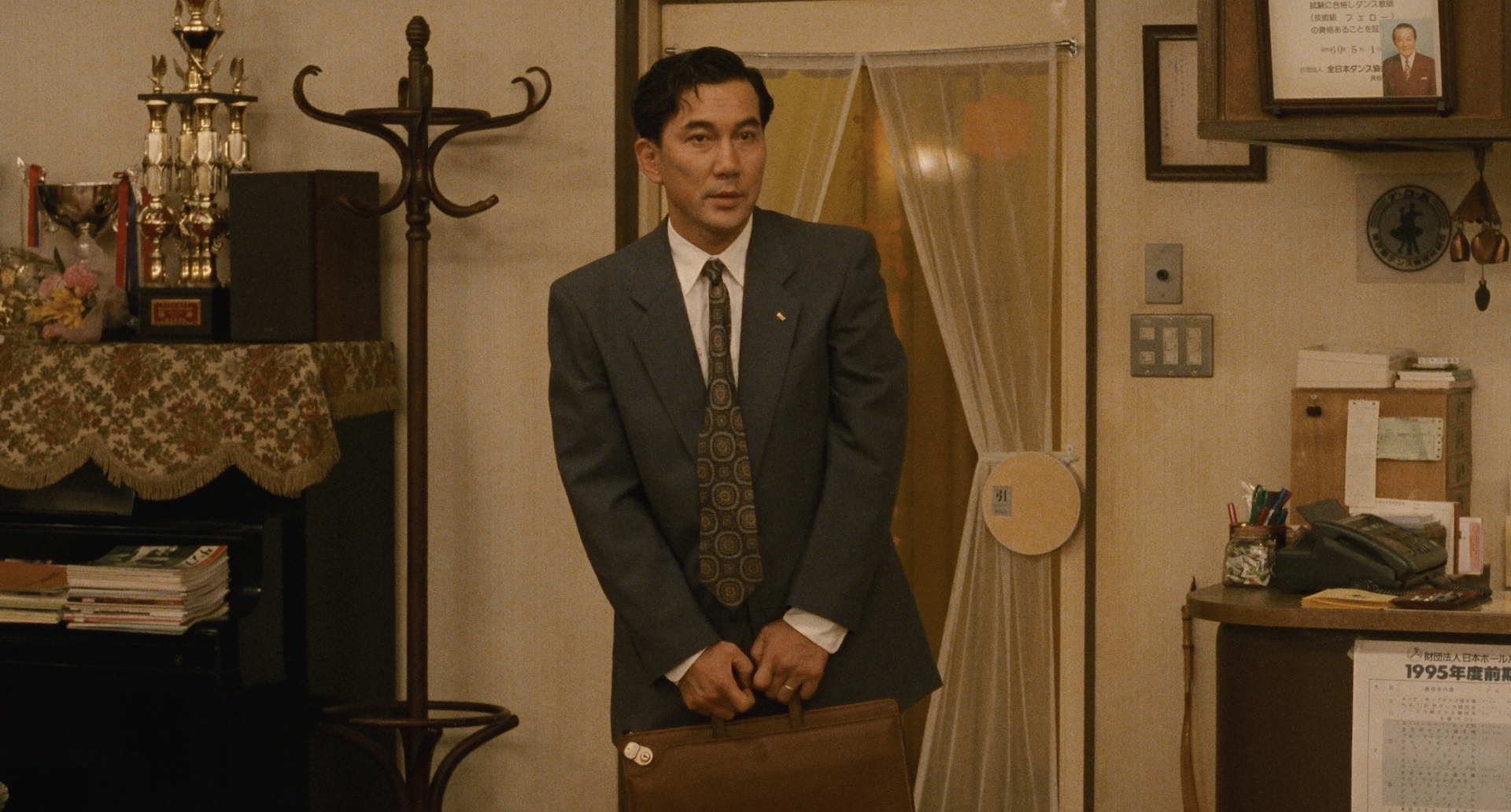Koji Yakusho as Shohei Sugiyama hesitates with his briefcase at the door of a dance school in Shall We Dance? (1996)