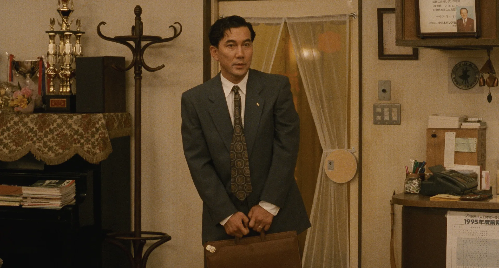 Koji Yakusho as Shohei Sugiyama hesitates with his briefcase at the door of a dance school in Shall We Dance? (1996)