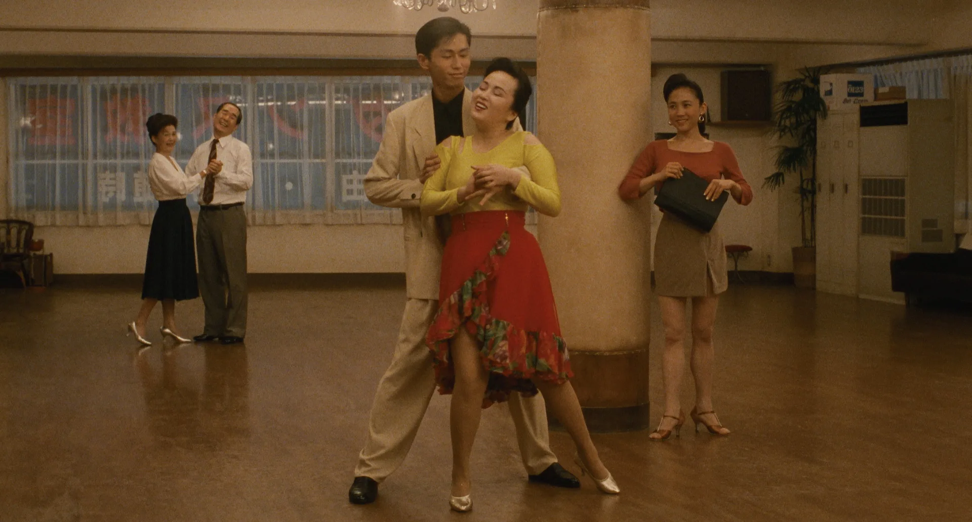 A young instructor leads an older student across the dance-school floor in Shall We Dance? (1996)