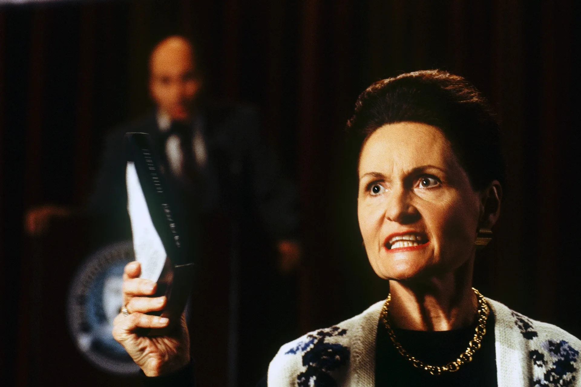 A woman brandishes a book during a heated town meeting in Donnie Darko (2001)