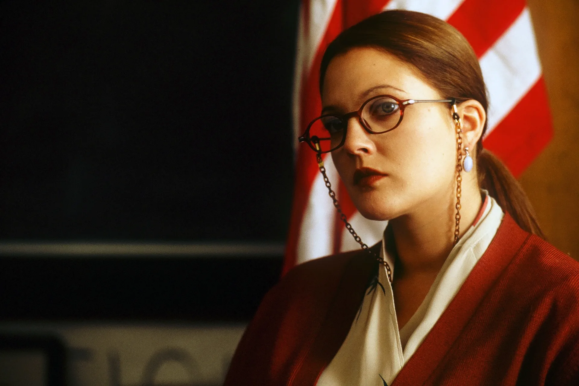 A schoolteacher in round glasses stands before an American flag in Donnie Darko (2001)