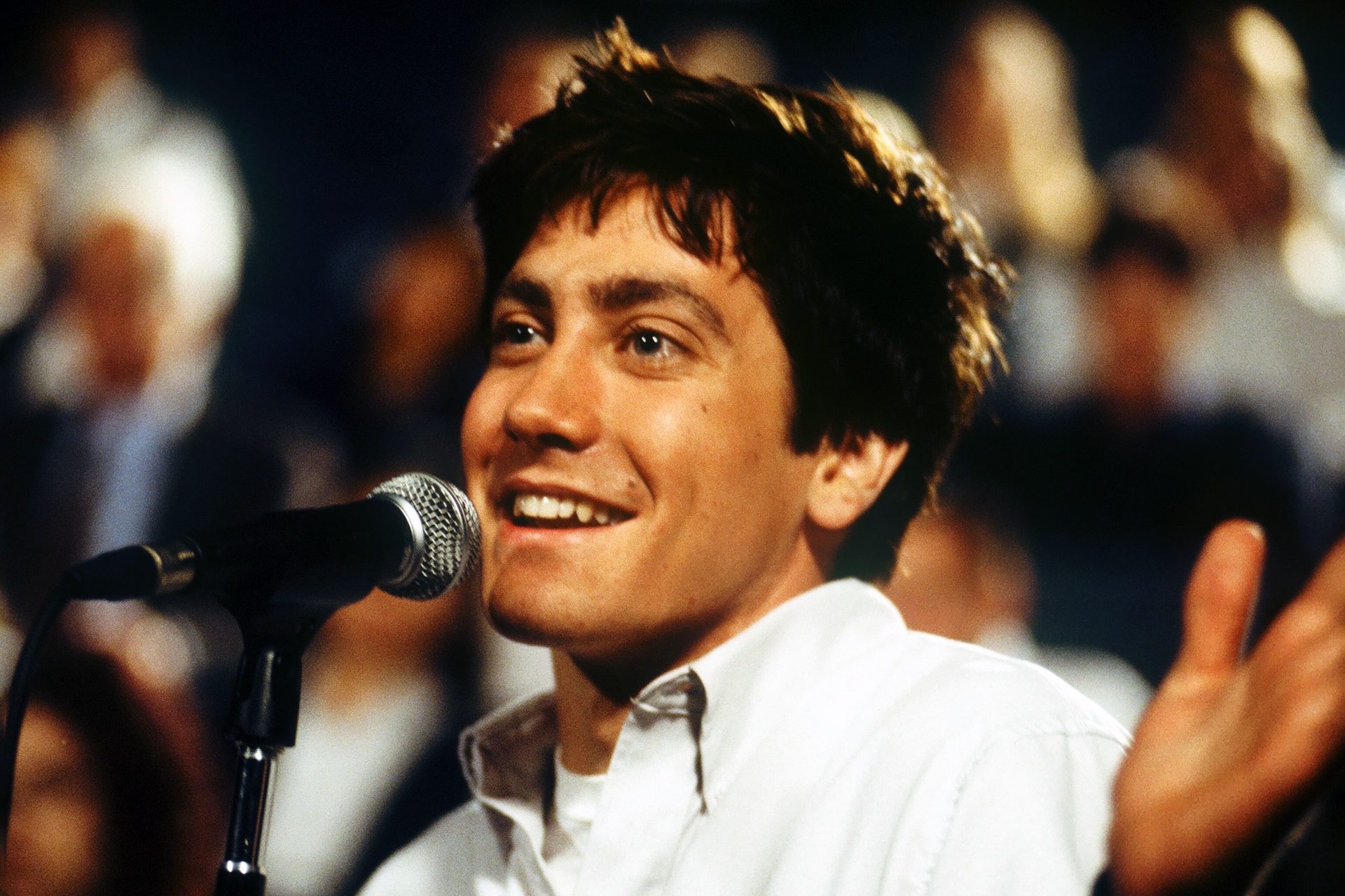 Jake Gyllenhaal as Donnie grins at a microphone before a seated audience in Donnie Darko (2001)