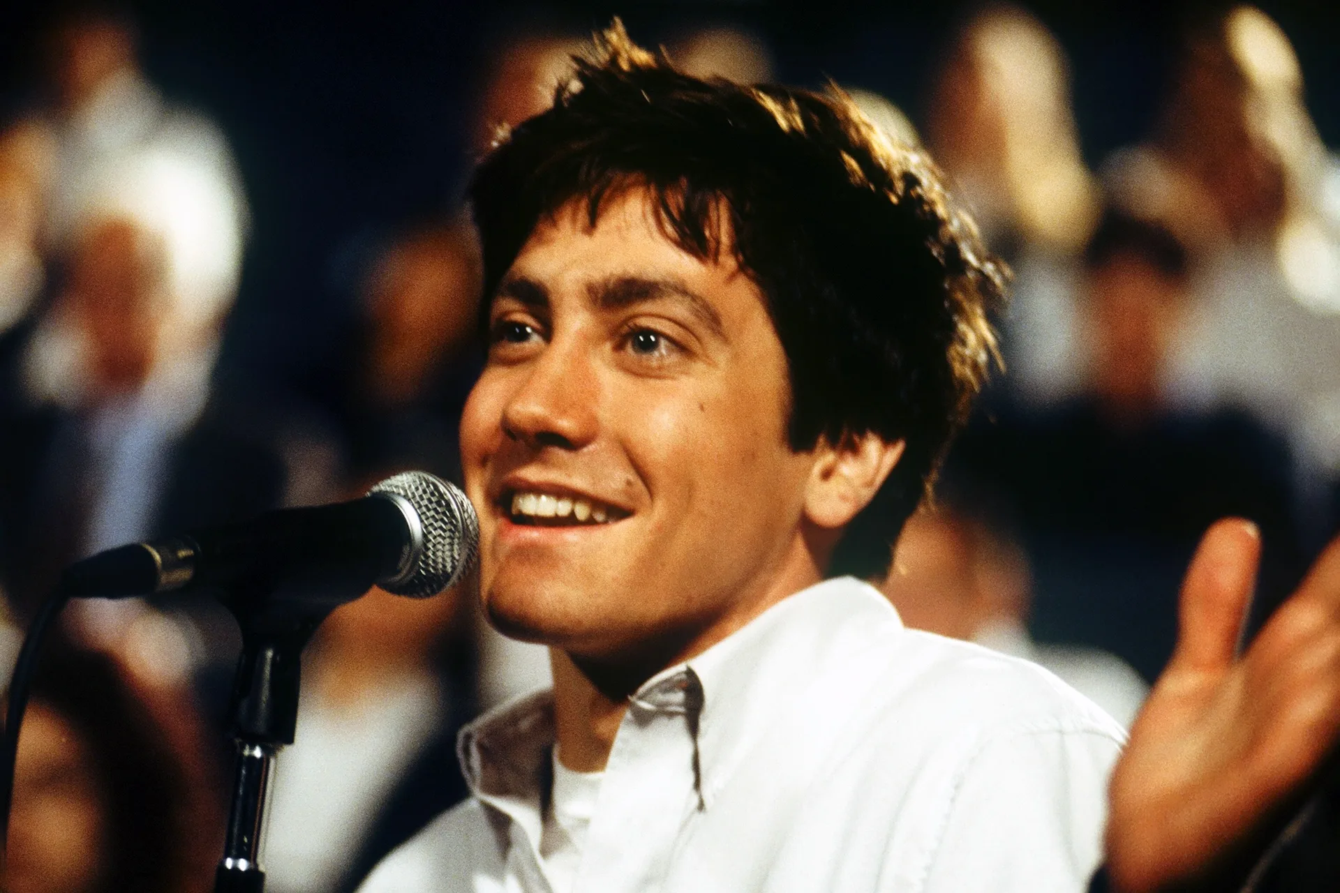 Jake Gyllenhaal as Donnie grins at a microphone before a seated audience in Donnie Darko (2001)