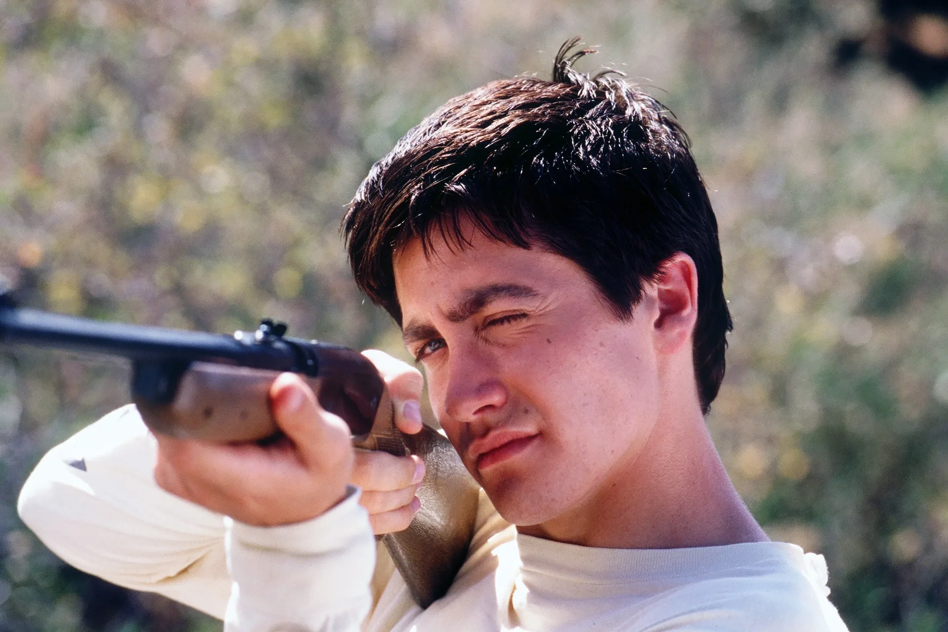 Jake Gyllenhaal as Donnie takes aim with a rifle in the open countryside in Donnie Darko (2001)