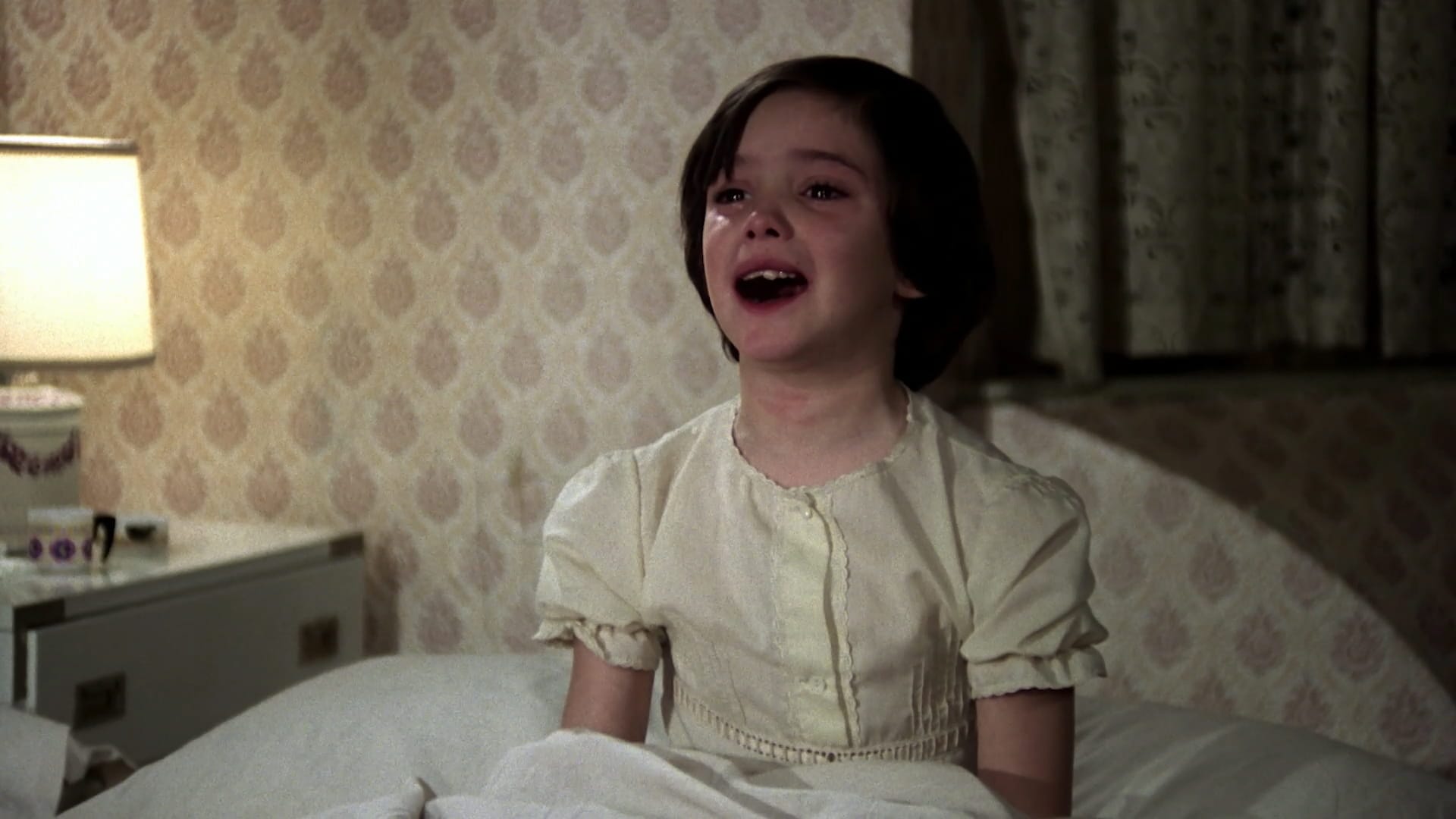 Ana cries sitting up in bed in her nightdress in Cría Cuervos