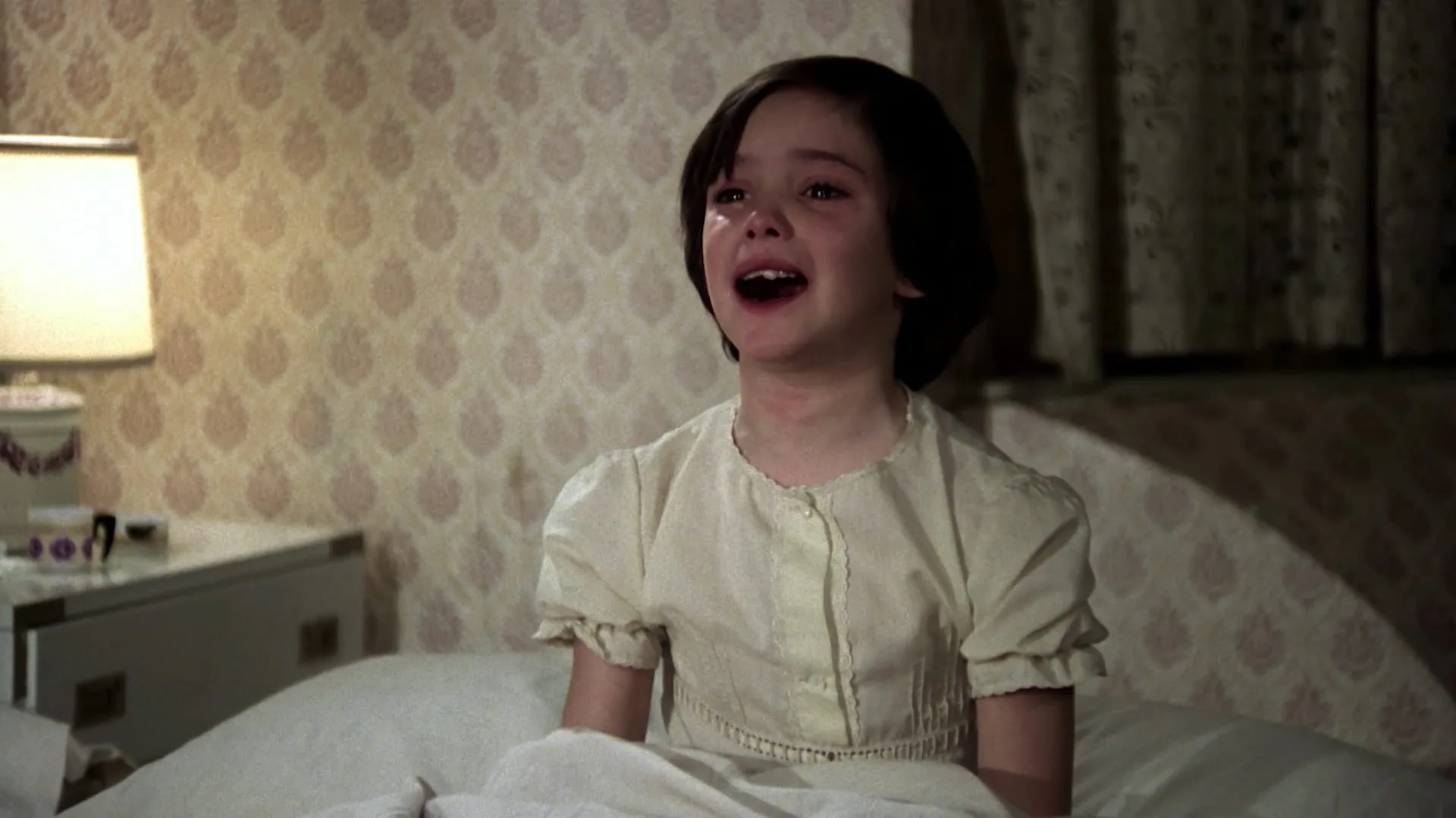 Ana cries sitting up in bed in her nightdress in Cría Cuervos