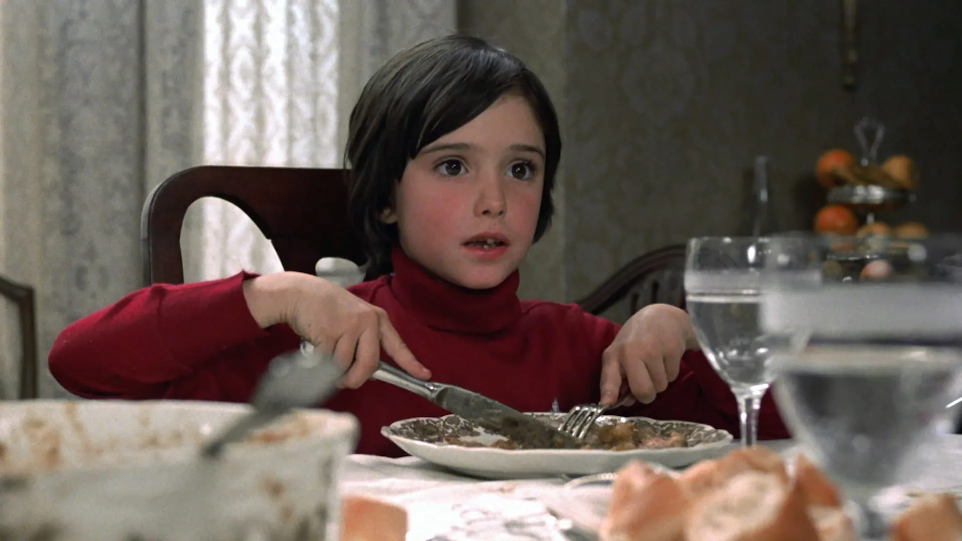 Ana Torrent in a red turtleneck eating at the family dining table in Cría Cuervos