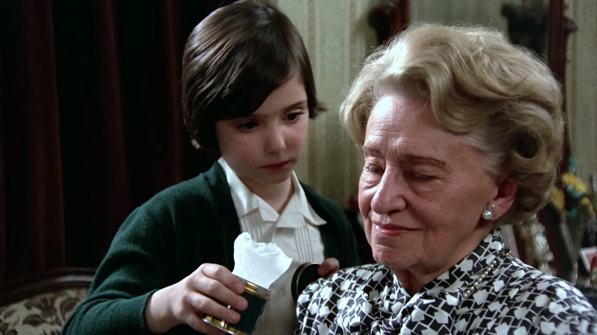 Ana sits beside her grandmother holding a tin of keepsakes in Cría Cuervos