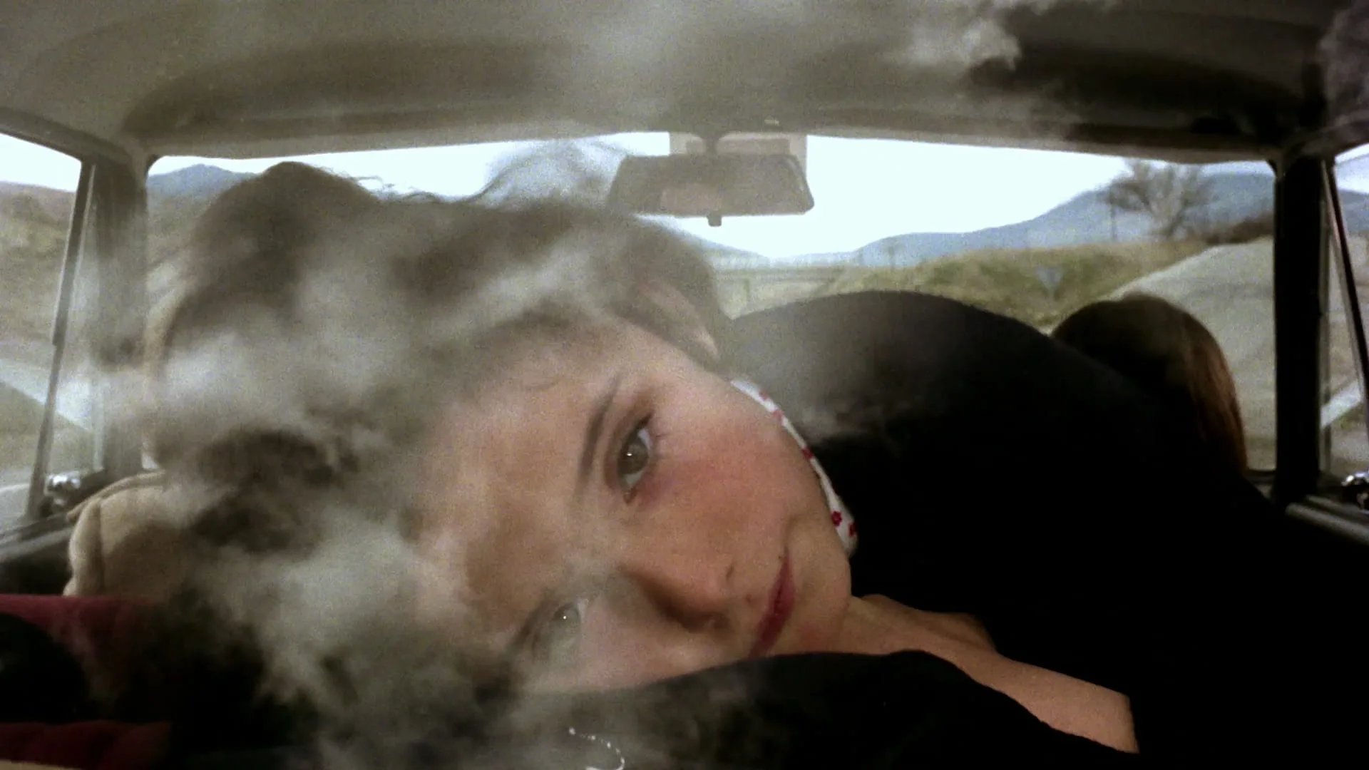 A woman's face glimpsed inside a car through drifting dust in Cría Cuervos