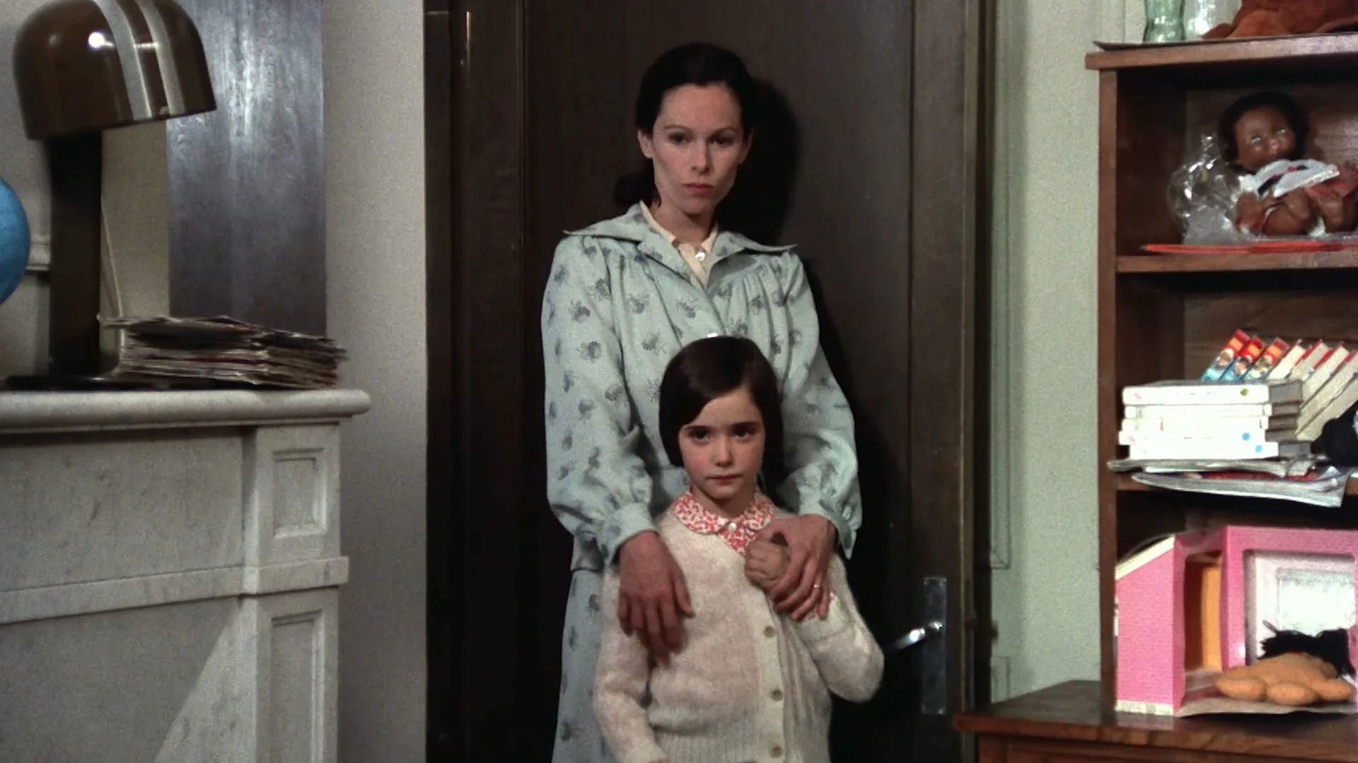 Geraldine Chaplin stands behind Ana Torrent with hands on her shoulders in a doorway in Cría Cuervos