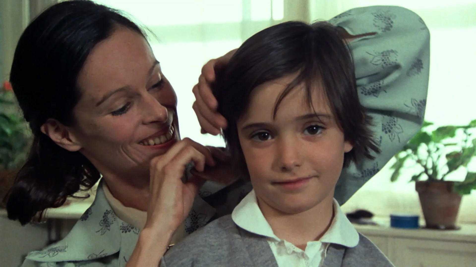 Ana's mother (Geraldine Chaplin) smiles while fixing Ana's hair by a bright window in Cría Cuervos