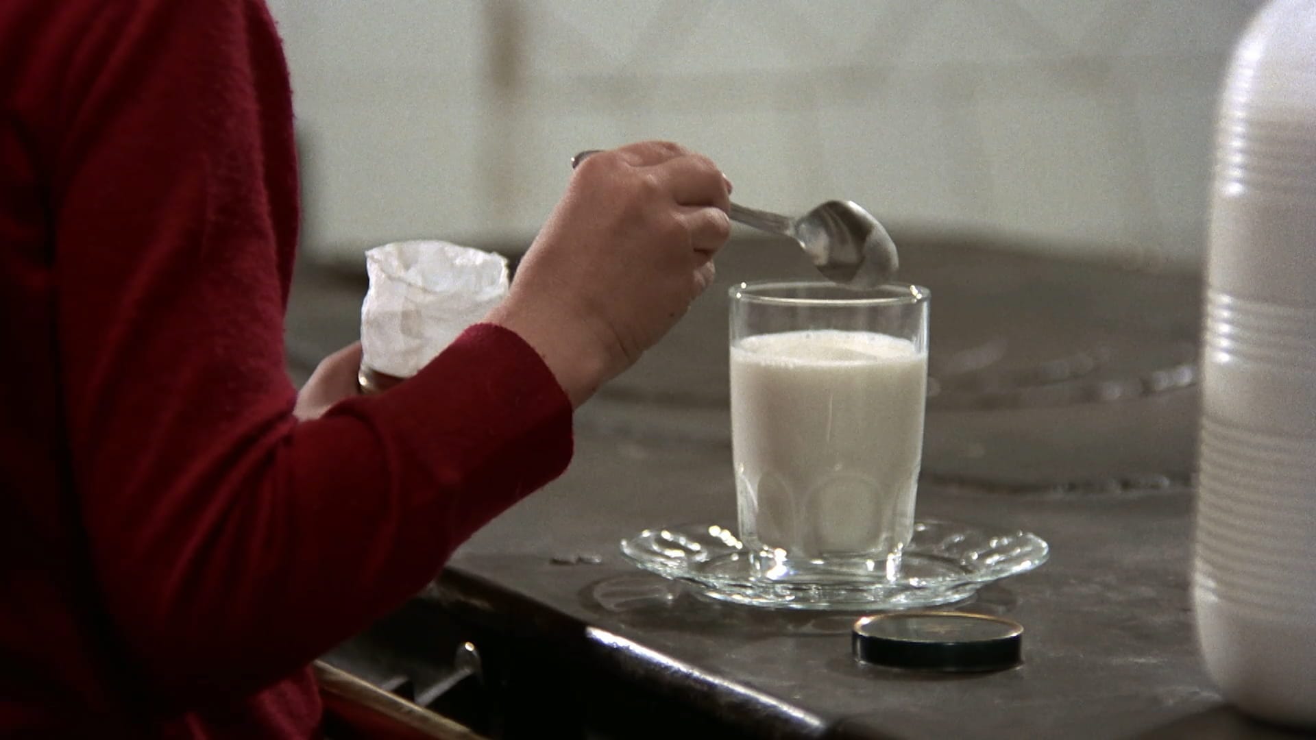 Close-up of Ana spooning powder into a glass of milk in Cría Cuervos
