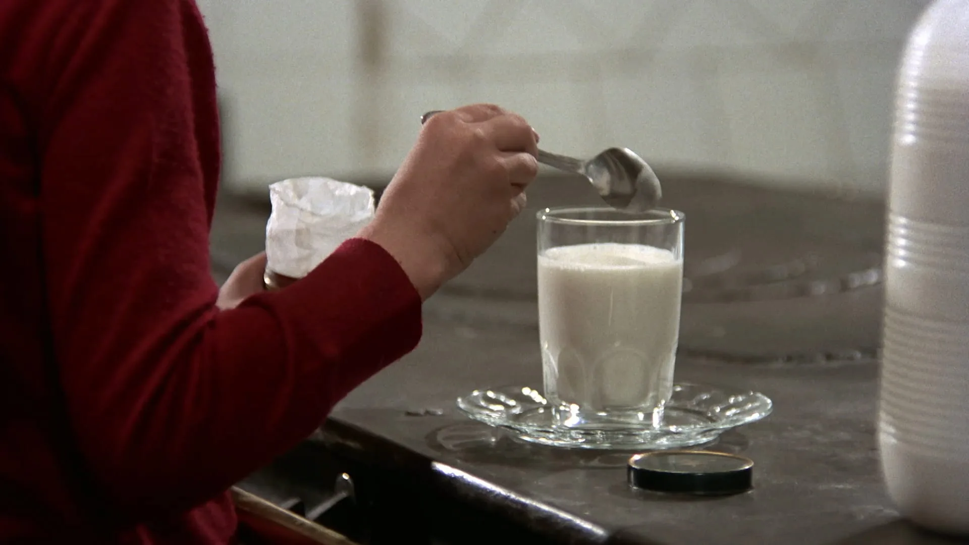 Close-up of Ana spooning powder into a glass of milk in Cría Cuervos