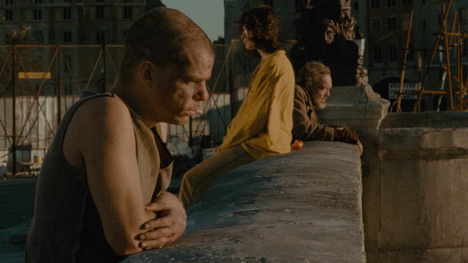 Denis Lavant as Alex leans on the parapet of the Pont-Neuf with a cigarette, while Michèle sits on the wall and Klaus-Michael Grüber as Hans looks out beside her, in Les Amants du Pont-Neuf (1991)