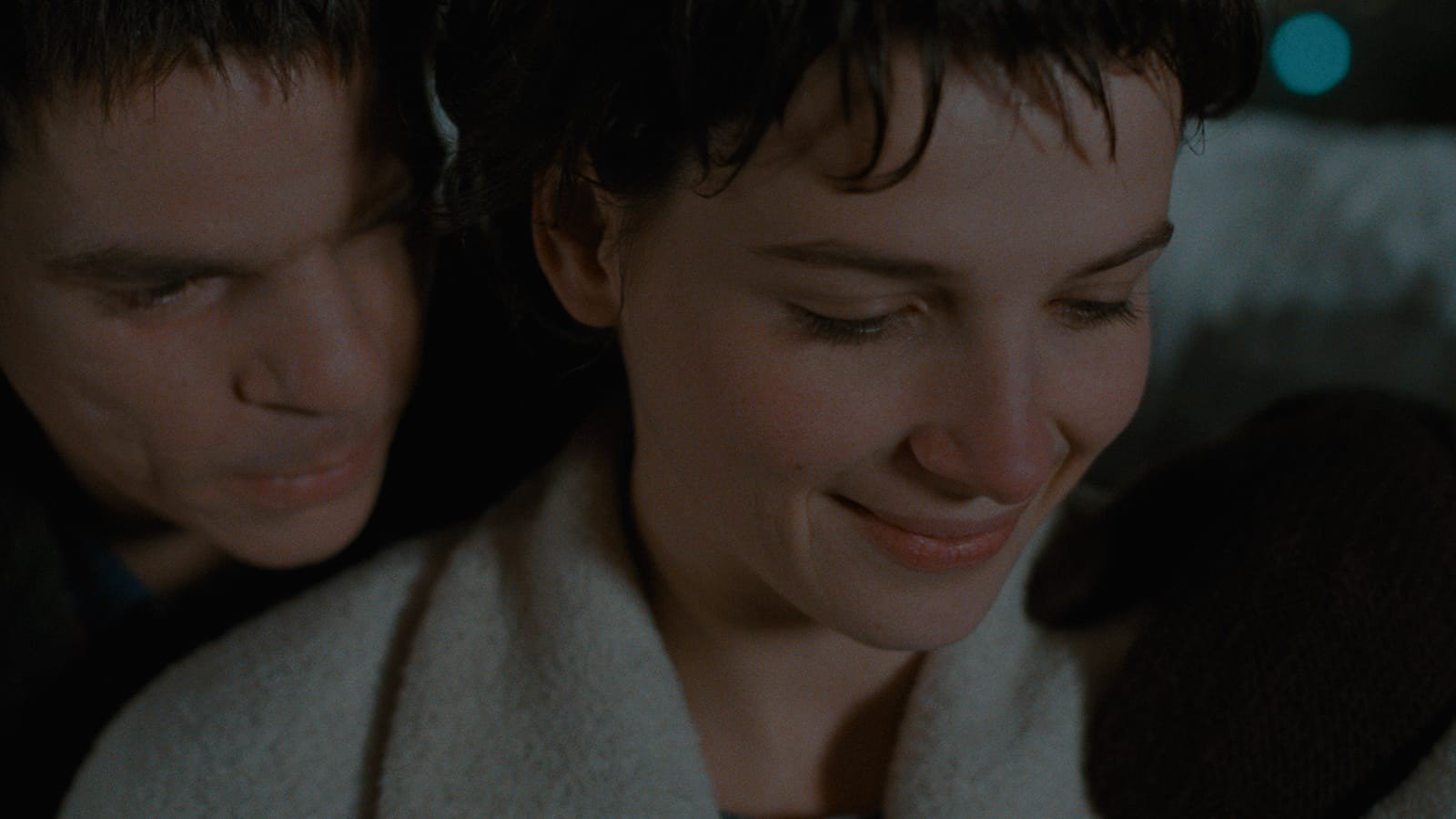 Juliette Binoche as Michèle smiles down, wrapped in a pale blanket, as Denis Lavant as Alex leans in over her shoulder in Les Amants du Pont-Neuf (1991)